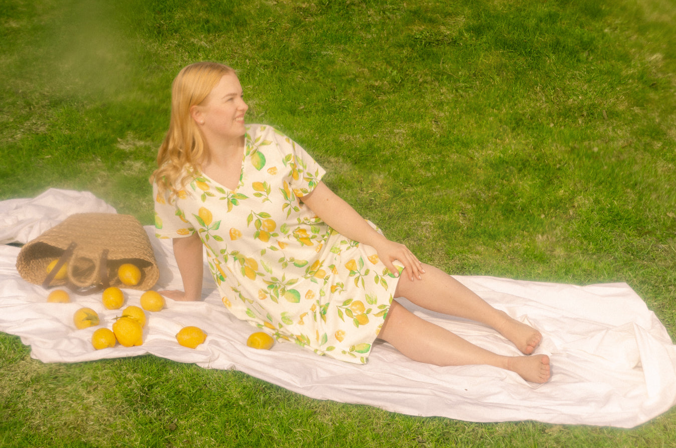 Nainen istuu nurmikolla päällään Toiveen v-pääntiemekko Limone kuosissa.