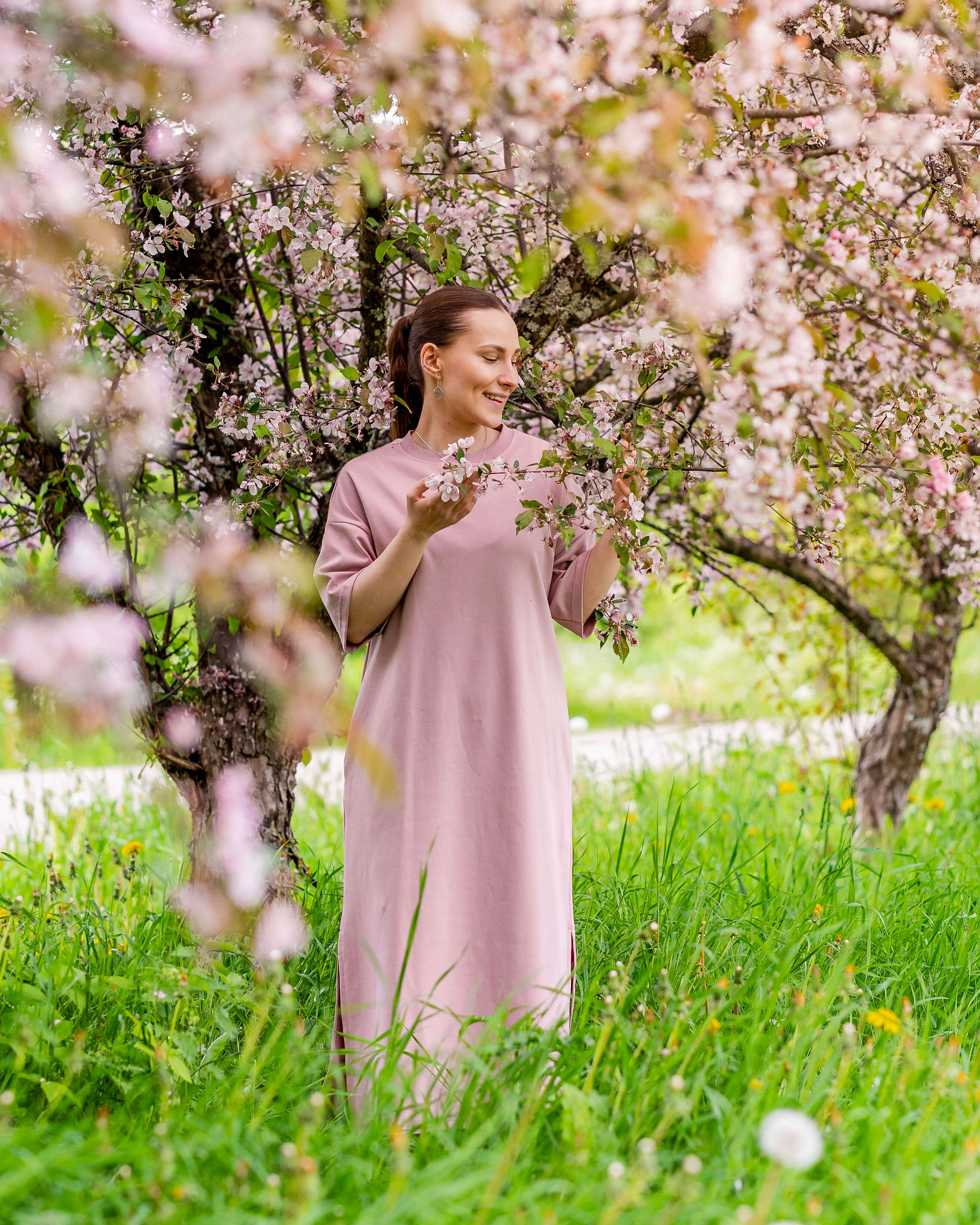 Nainen seisoo omenapuun alla päällään Toiveen boxymekko sävyssä roosa.