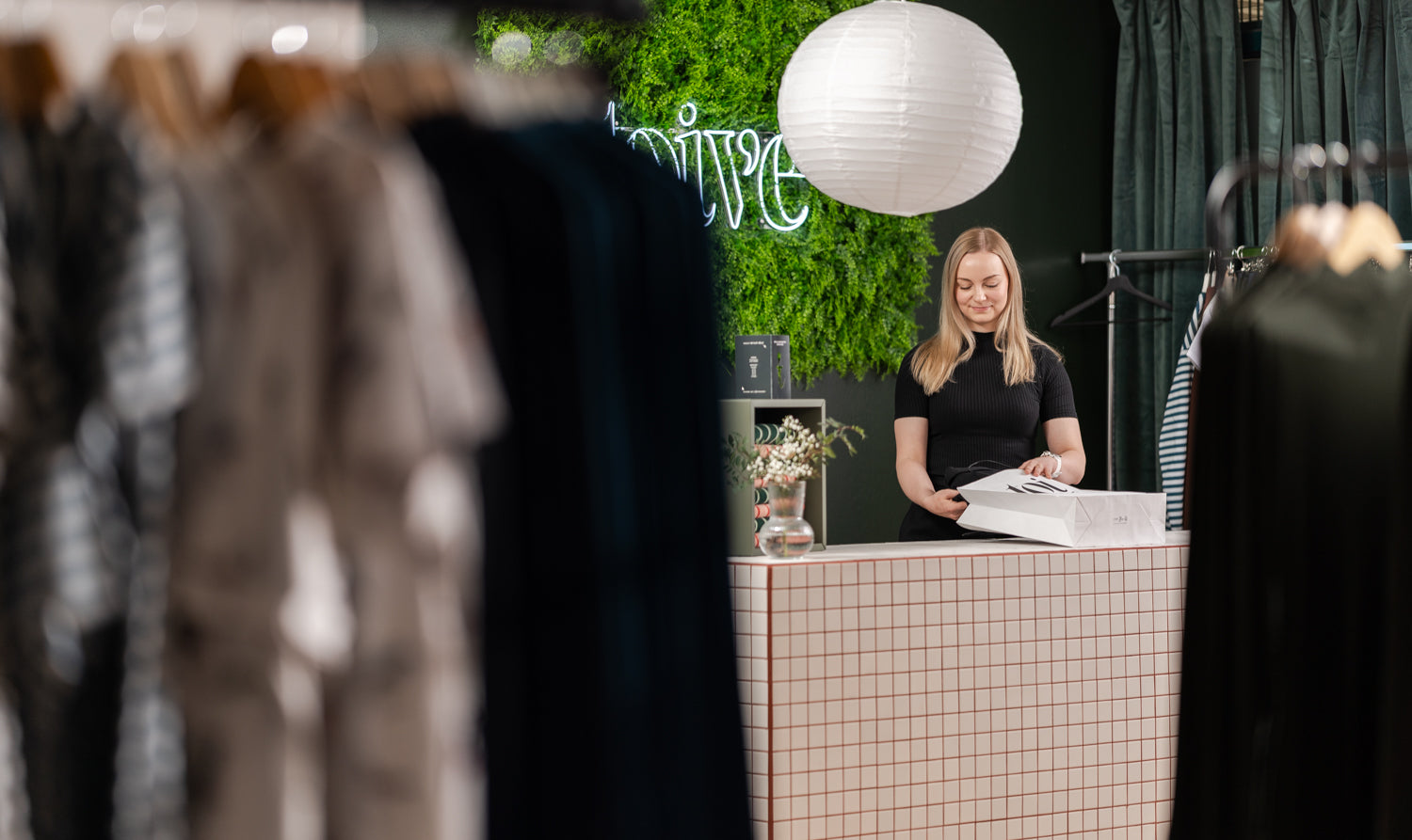 Myyjä tiskin takana laittamassa vaatteita paperikassiin.